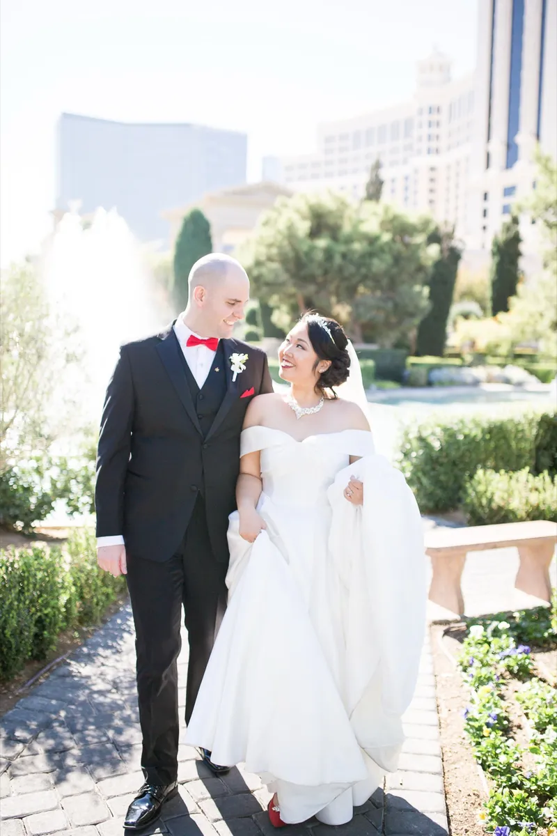Bride and groom walking together past the fountain, the groom holding her train off the stone
