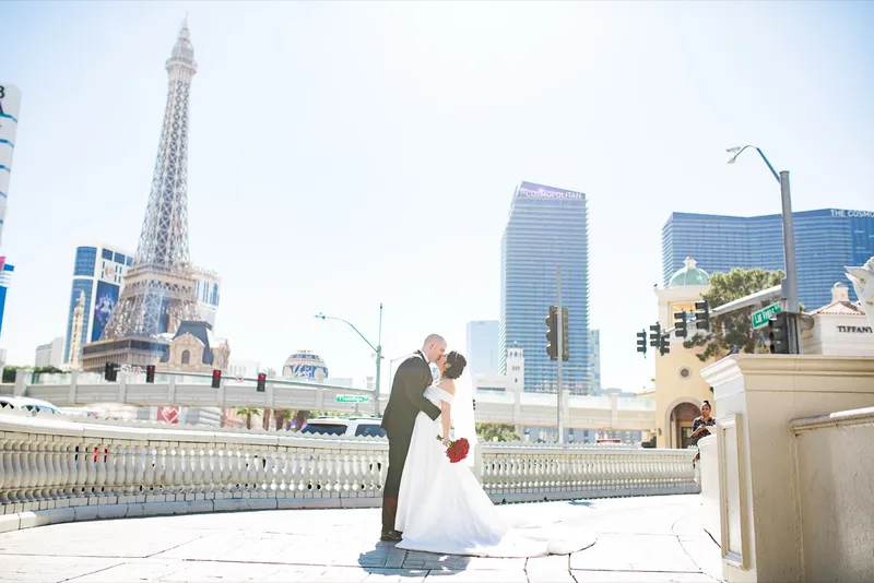 Bride and groom kissing on a raised walkway above the street with the Strip skyline and the Eiffel Tower replica behind them