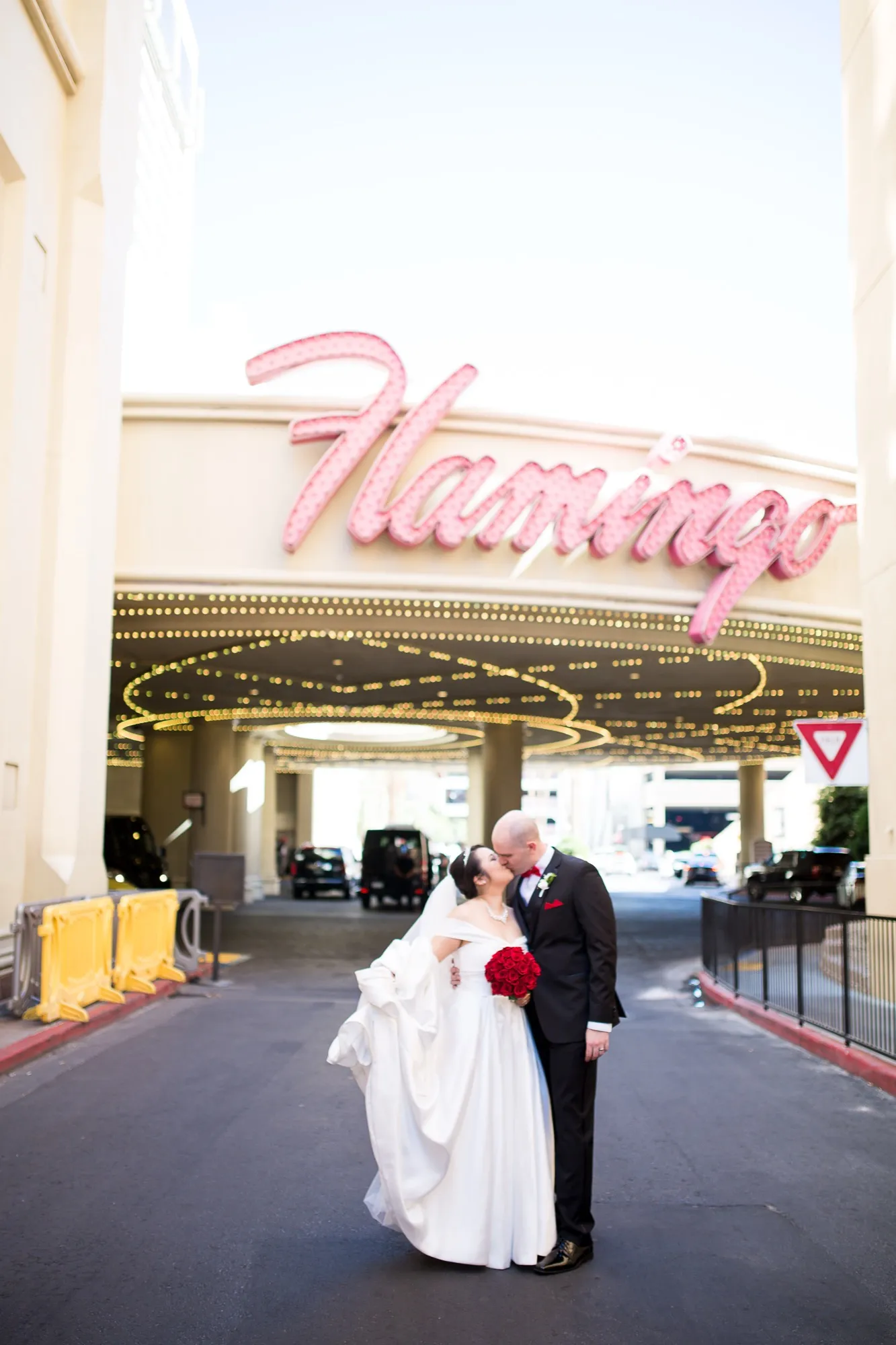 A bride and groom kiss beneath the Flamingo’s pink neon script sign, its canopy of lights glowing behind them