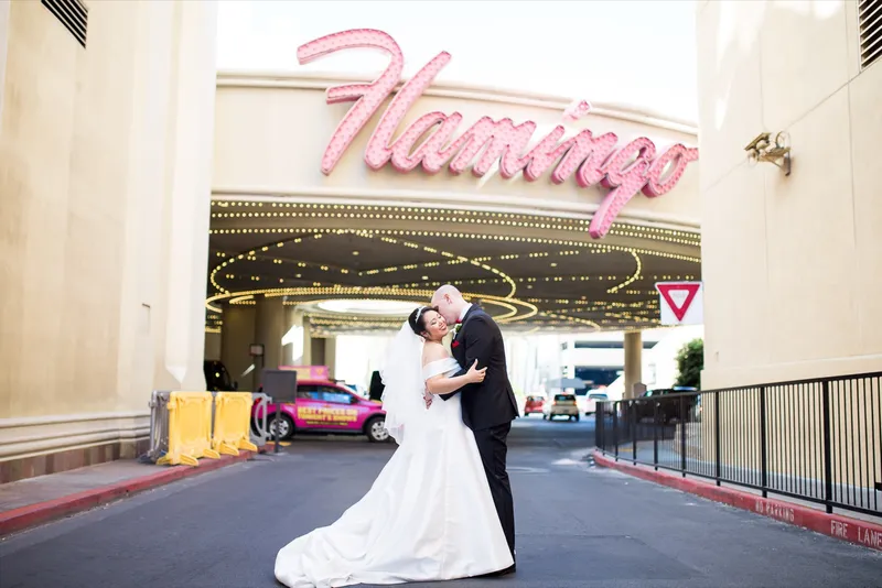 Bride and groom embracing on the drive under the resort's pink neon script sign and its canopy of light bulbs