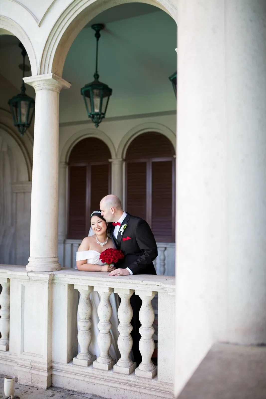 Bride and groom leaning on a stone balustrade under the arches, green iron lanterns hanging overhead