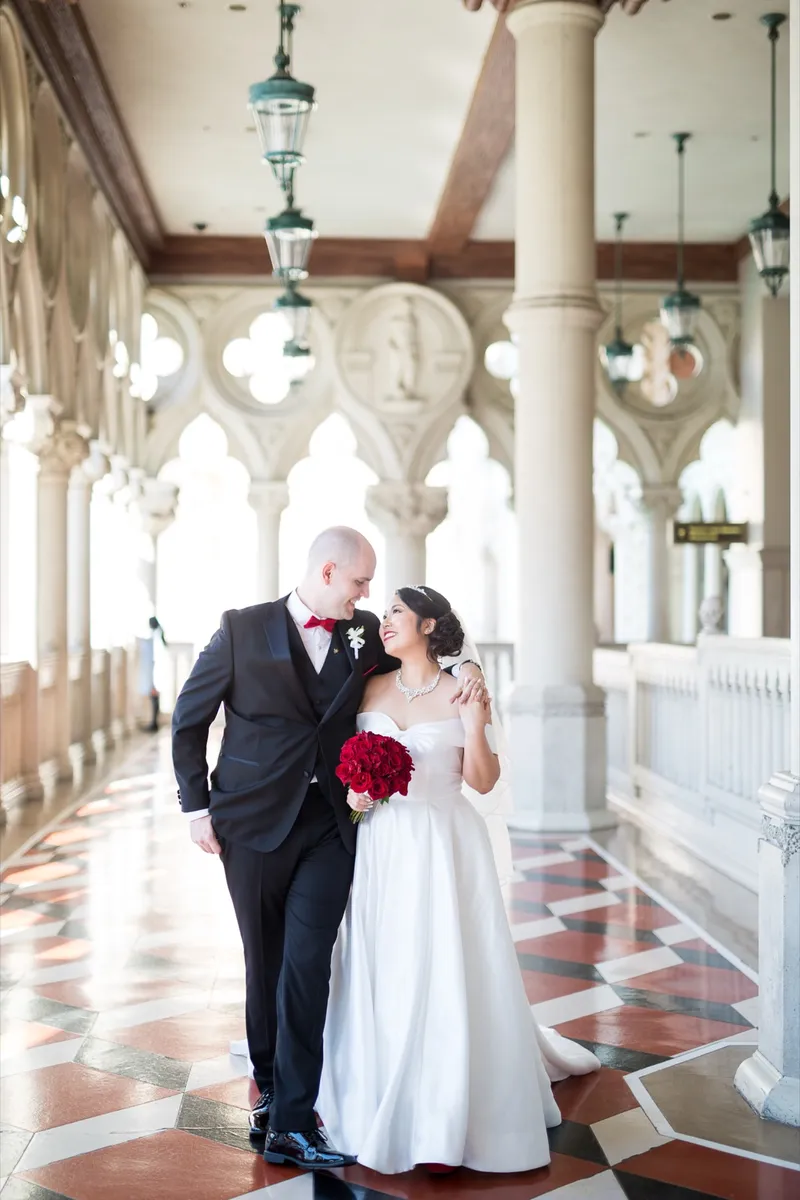 Bride and groom walking the length of the colonnade together, her red roses held down at her side
