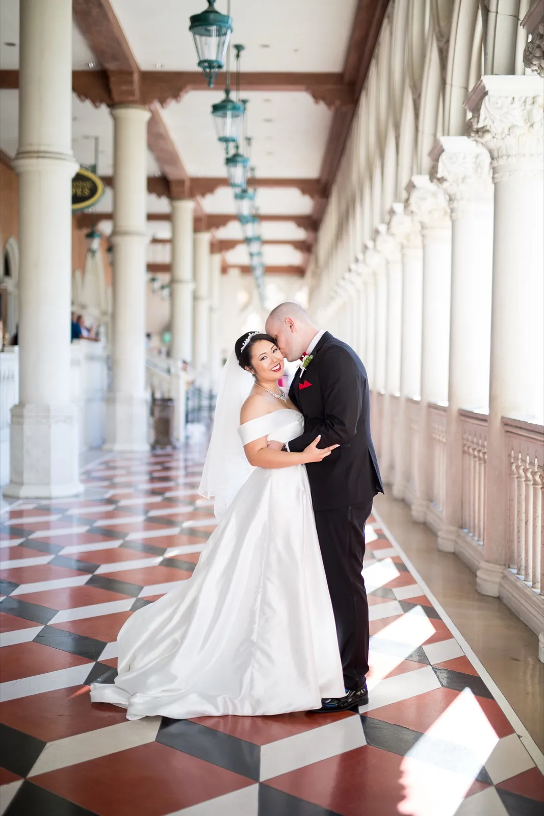 Bride and groom standing full length on the diamond patterned marble, sunlight falling in patches nearby