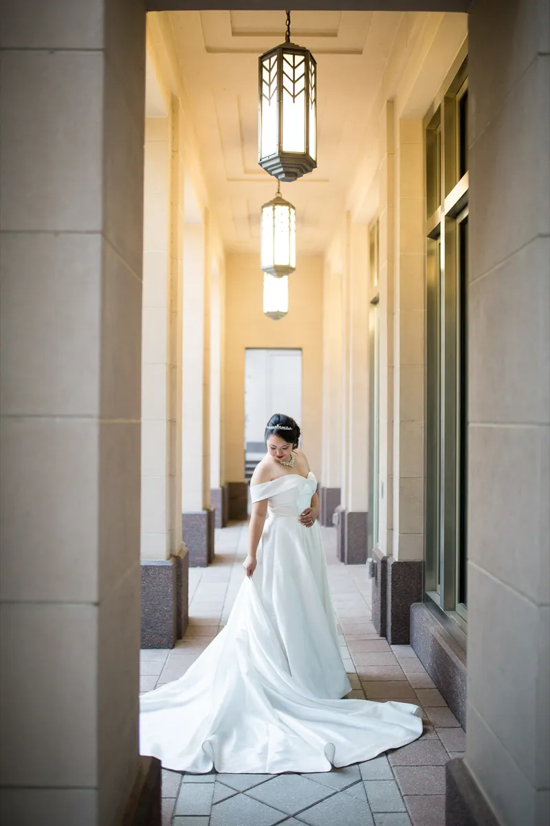 Bride further down the colonnade looking over her shoulder with the train of her satin gown spread across the tile