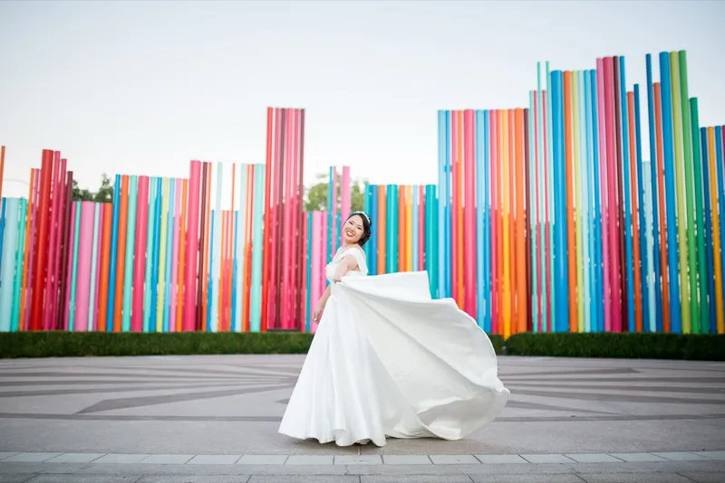 Bride sweeping the full skirt of her satin gown out in front of the wall of colored pipes
