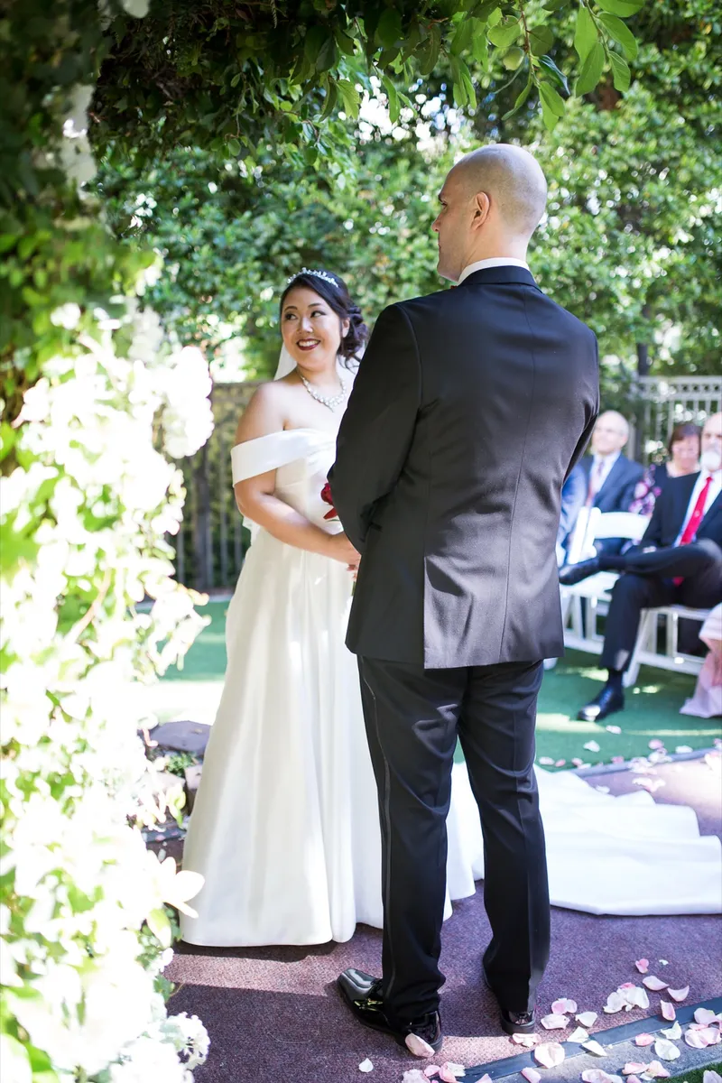 Bride and groom standing together at the ivy arch during the ceremony with guests seated behind them