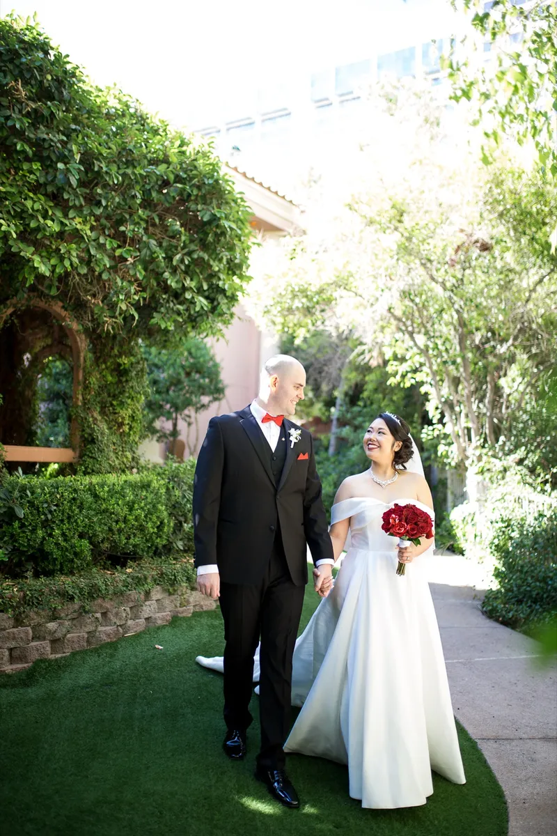 Bride and groom walking the garden path together with palm trunks and the resort tower behind them
