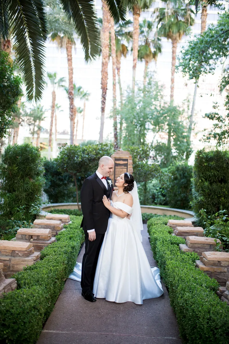 Bride and groom facing each other on the low hedge lined path under tall palms