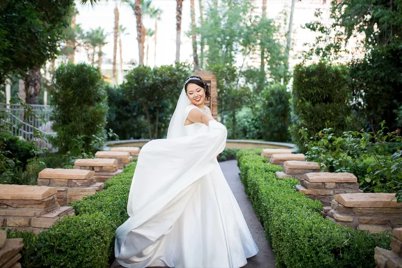 Bride swinging her full satin skirt out on the boxwood lined garden path with palms behind her