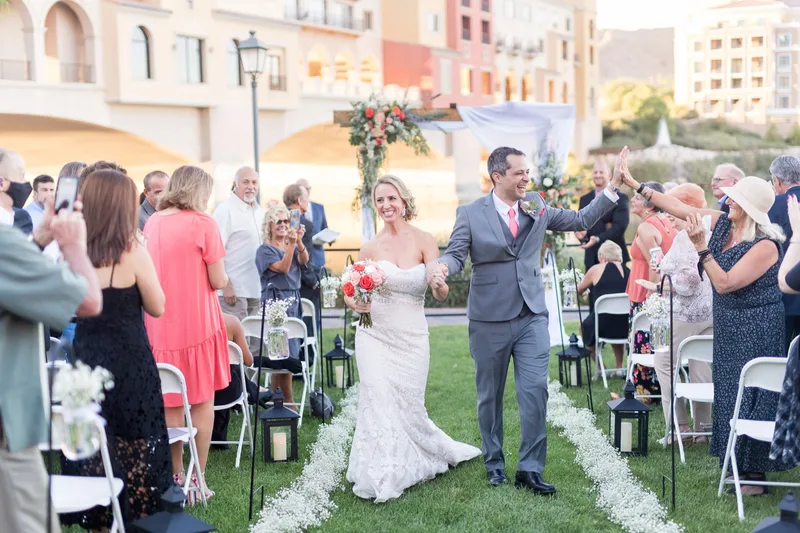 Couple walking back up the aisle to cheering guests with the lake behind the arch