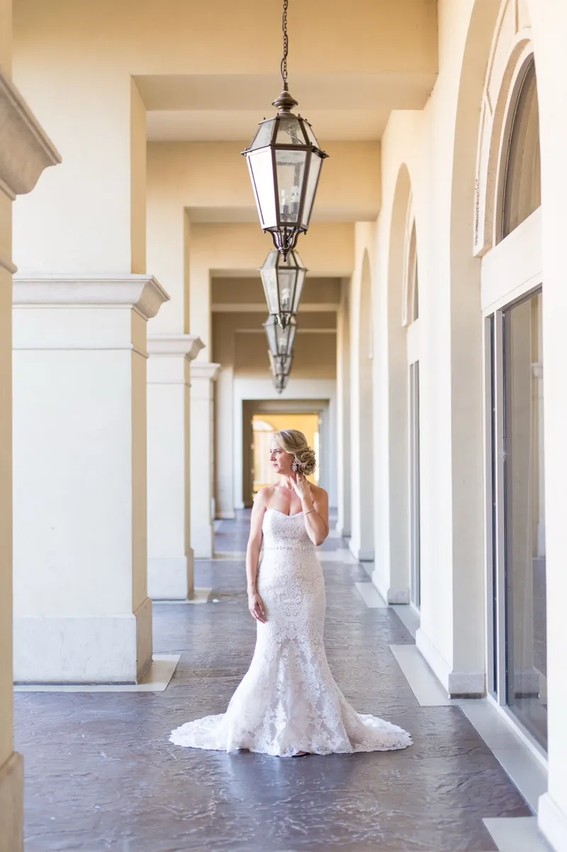 Bride standing alone between the arches with the train of her fitted lace gown fanned out behind her