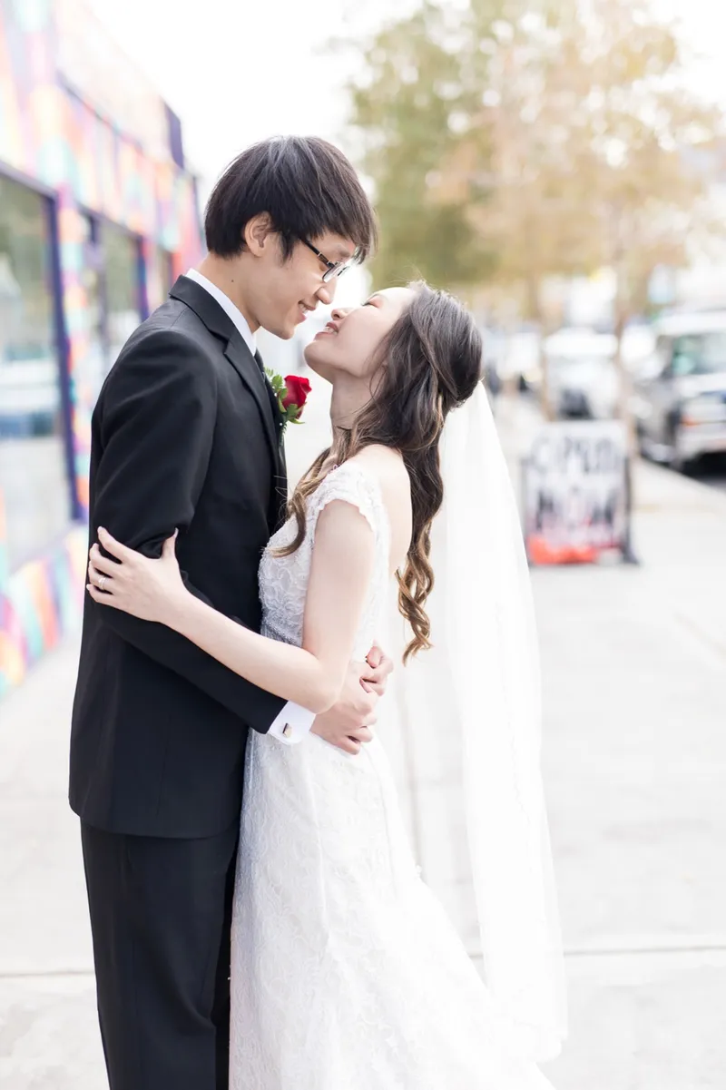 Couple holding each other close on the sidewalk in front of a painted storefront wall