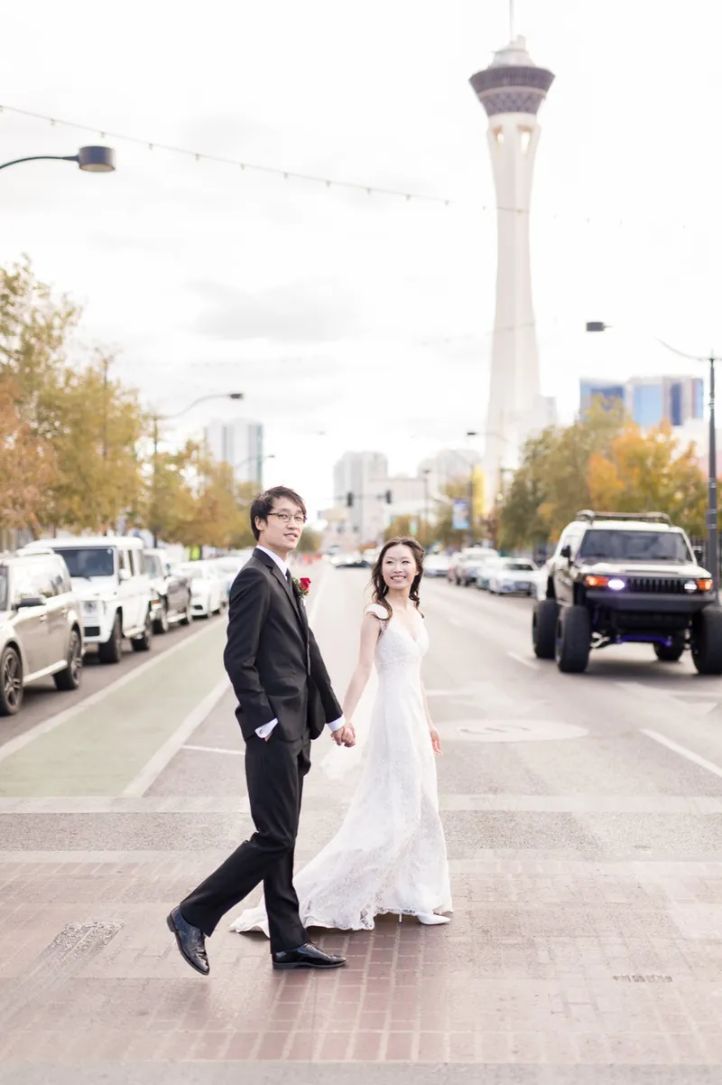 Bride and groom standing together in the middle of a downtown street with the STRAT tower rising behind them