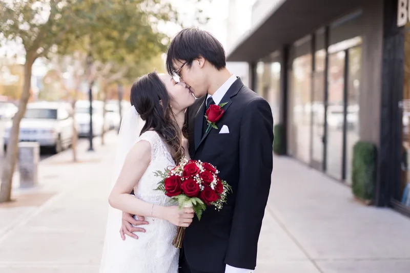 Bride and groom kissing with her red rose bouquet held between them