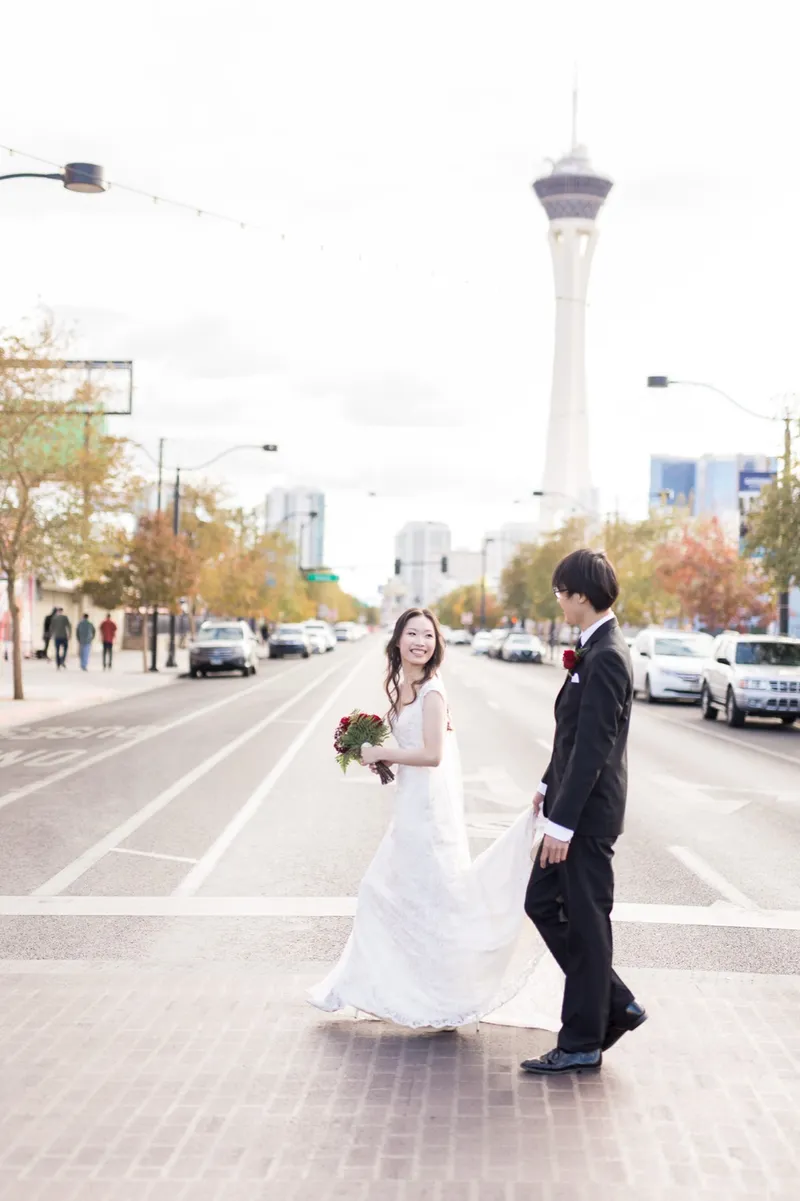 Couple crossing a wide downtown street hand in hand with the STRAT tower far up the road