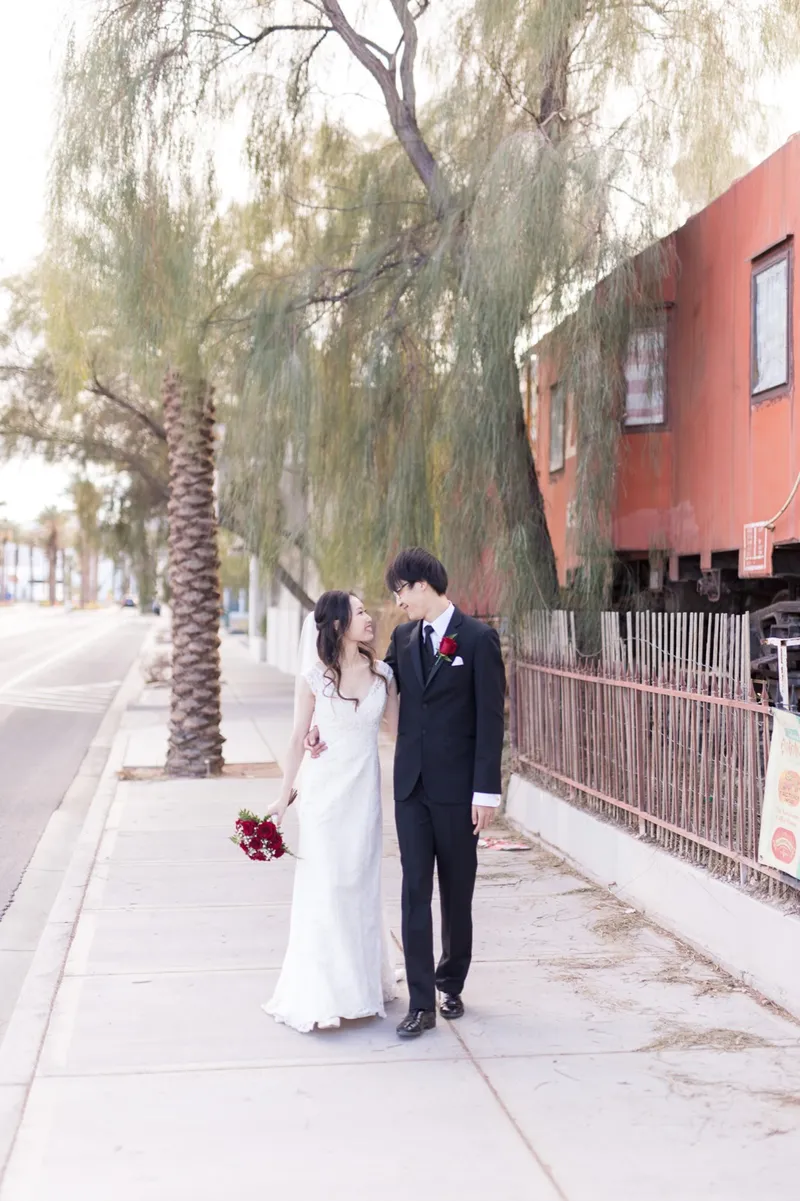 Couple walking a sidewalk under a willowy tree with palms on one side and the red railcar on the other