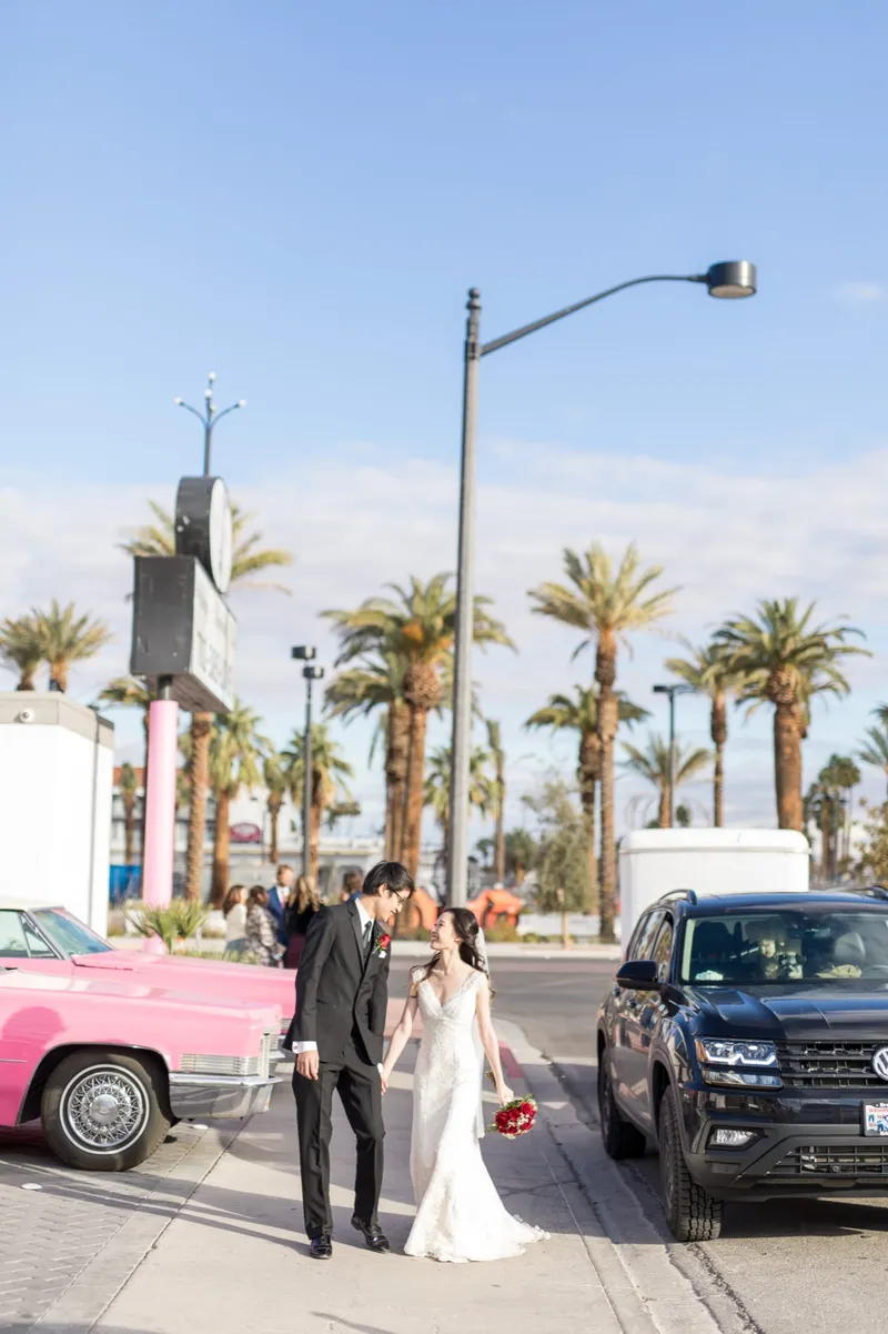 Bride and groom walking past a pink vintage Cadillac parked at the curb