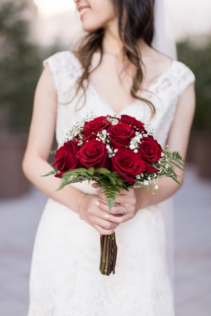 Bride holding a bouquet of deep red roses against her ivory lace gown, her face soft and out of focus above it