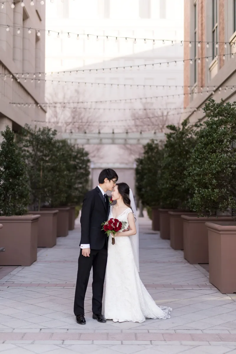 Couple kissing on the walkway between the planters, red roses in her hand and string lights overhead