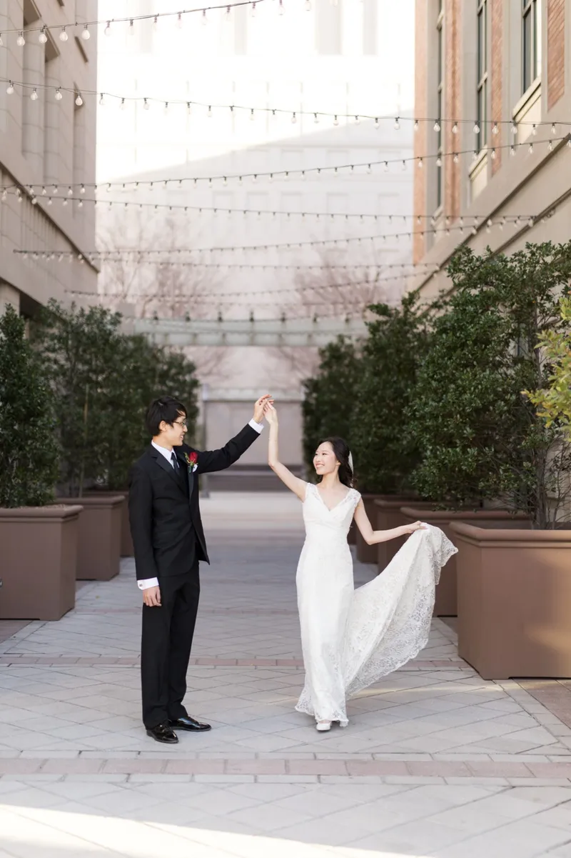 Groom turning his bride under his arm on the walkway, her lace train sweeping around behind her