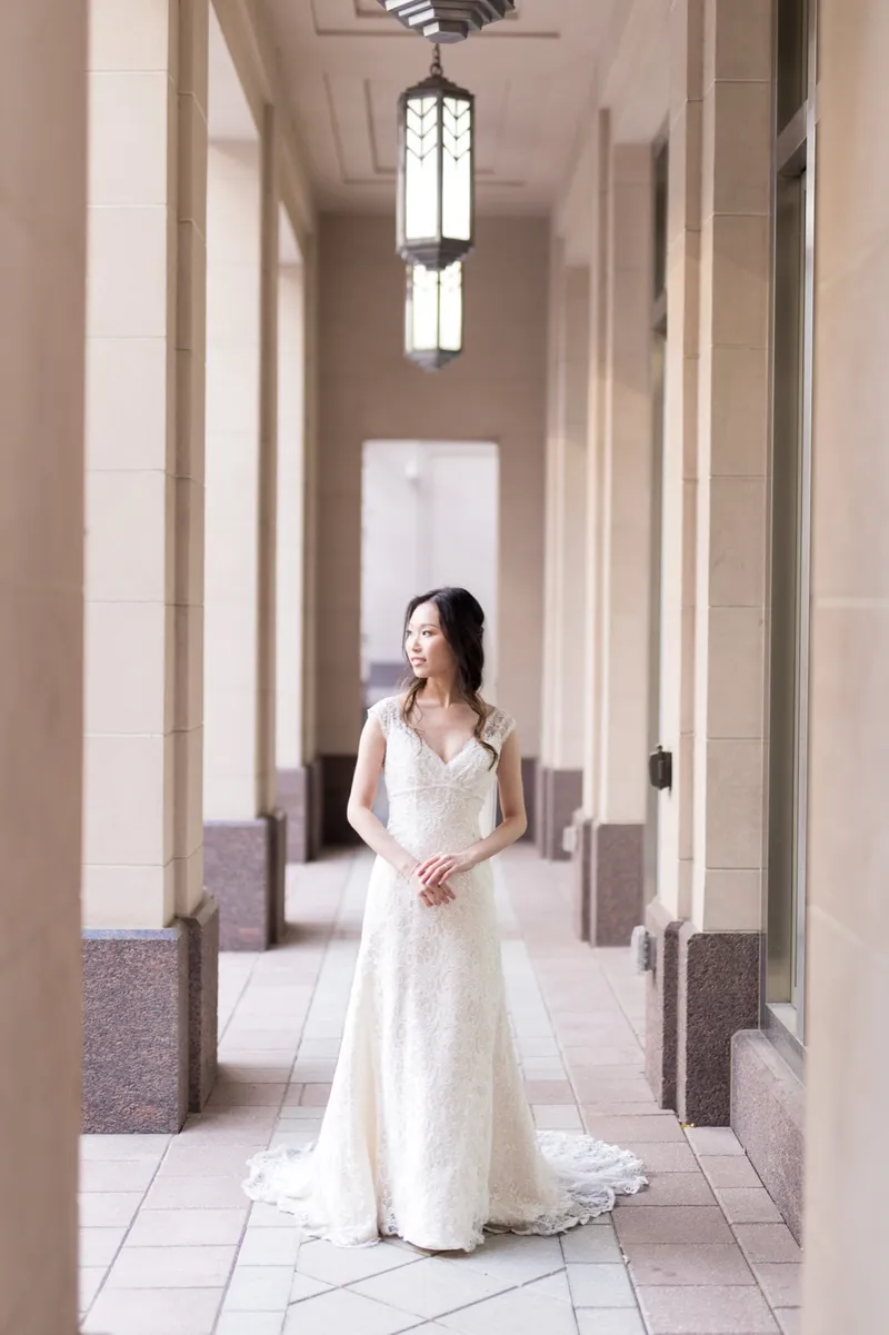 Bride alone in the lantern lit colonnade in a lace gown, her train trailing several feet behind her