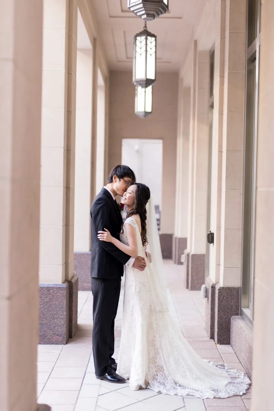 A groom kisses his bride’s forehead in the pale limestone colonnade at The Smith Center
