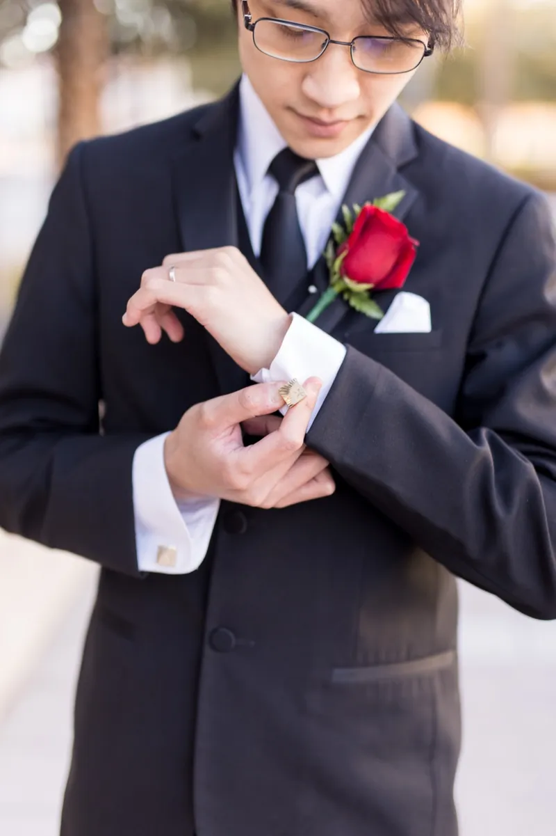 Close crop of a groom in a black suit fastening the cufflink on his left sleeve