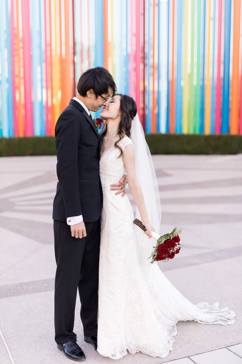 Bride and groom nose to nose and smiling in front of the pipes, her veil down her back and red roses in her hand