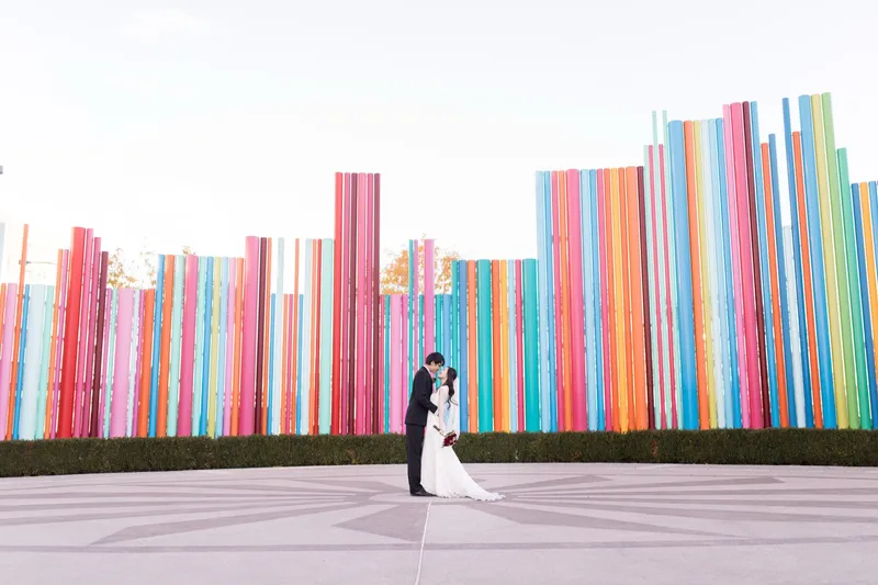 Wide view of the couple standing small against the full width of the colored pipe wall on the paved circle