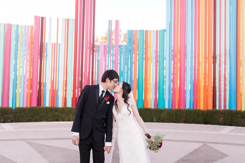 A bride and groom kiss in front of the tall colored pipes of the Pipe Dream sculpture in Symphony Park downtown