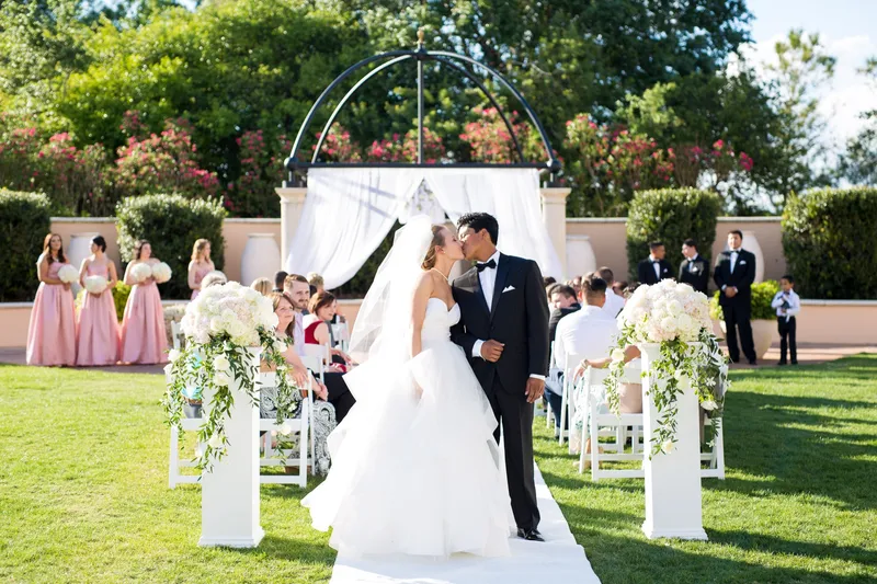 Bride and groom kissing at their garden ceremony surrounded by their wedding party