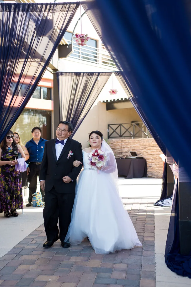 Bride coming through a navy draped entrance on an older man's arm as the ceremony begins