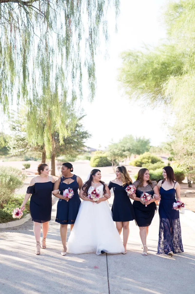 Bride and her bridesmaids in navy walking the shaded path together