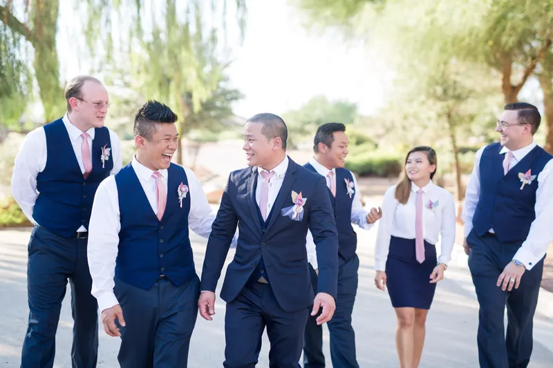 Groom walking with his groomsmen in navy vests and blush ties along the path