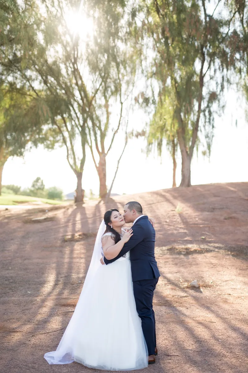 Couple kissing on the path with the sun breaking through the trees behind them