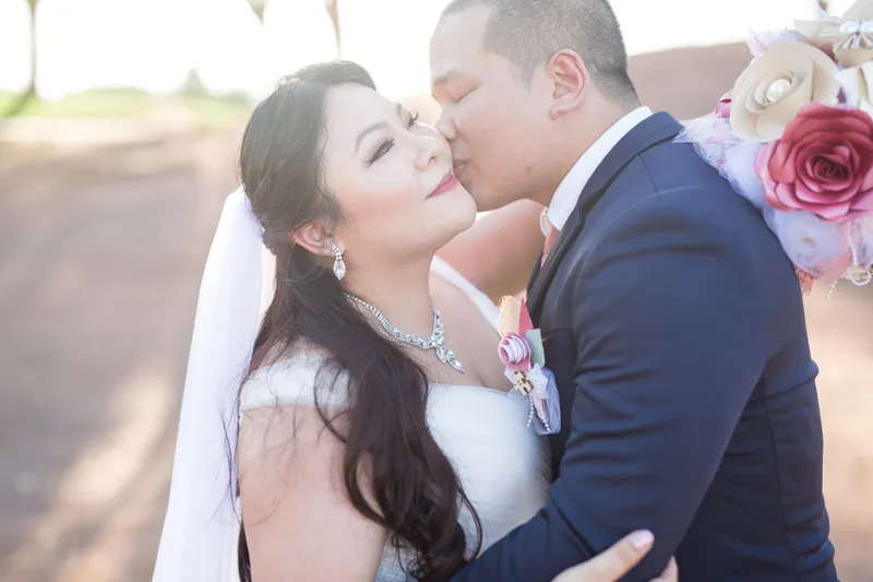 Groom kissing the bride's cheek in a close portrait, her handmade fabric bouquet resting over his shoulder