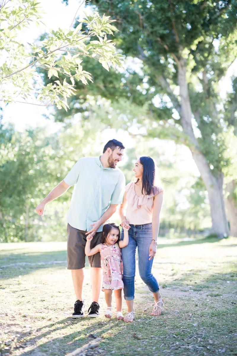 Couple walking a shaded path with their young daughter between them, each of them holding one of her hands