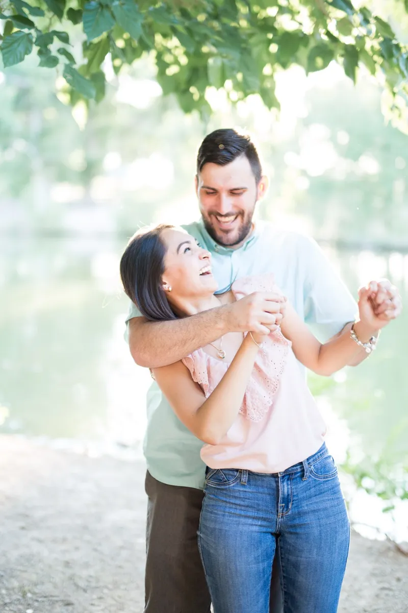 Couple laughing with their hands clasped at the edge of the pond under low green branches