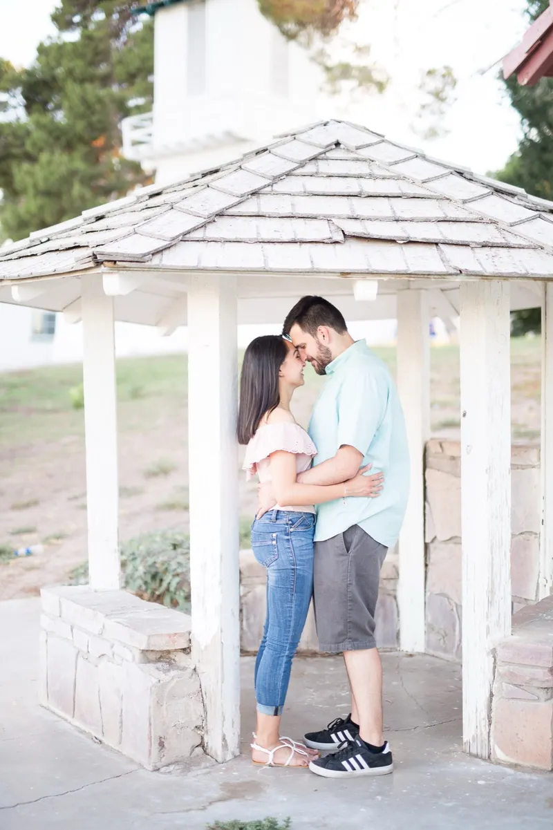 Couple standing forehead to forehead under a small park shelter with a shingled roof and a stone base