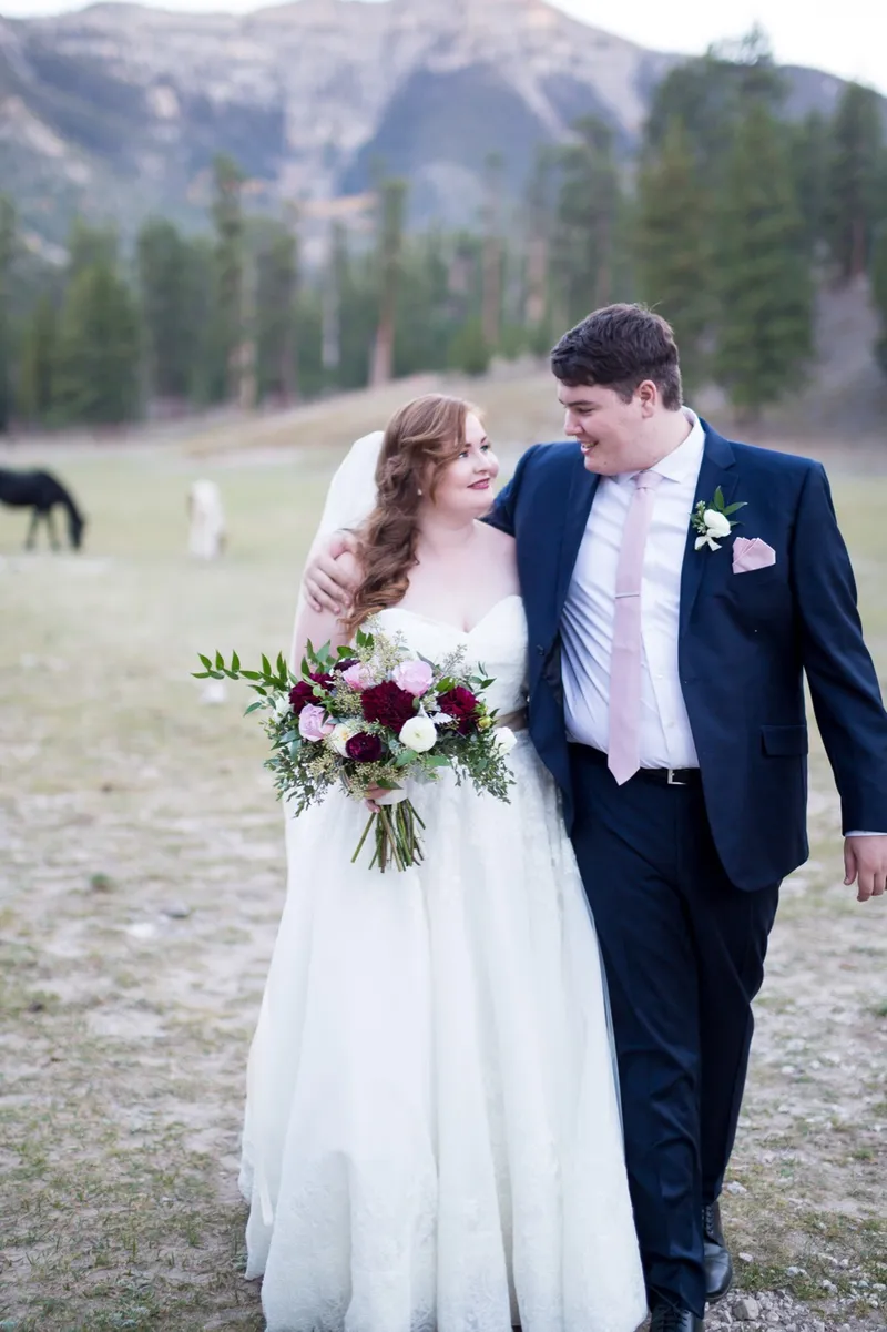 Bride and groom walking through the meadow together with her burgundy and blush bouquet