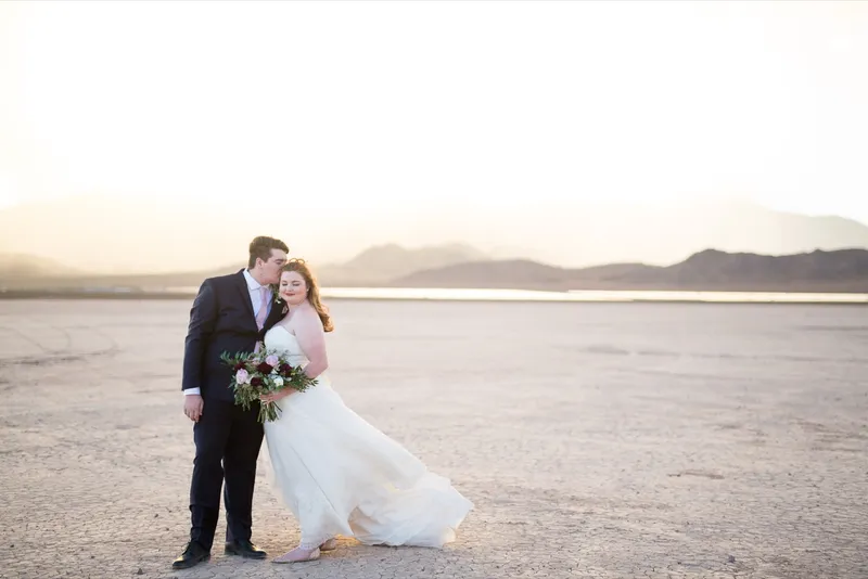 Bride and groom standing close together with her bouquet as the sunset spreads behind them