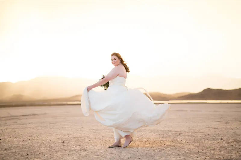 Bride swinging the skirt of her ivory ballgown as low gold sun floods the dry lake bed behind her