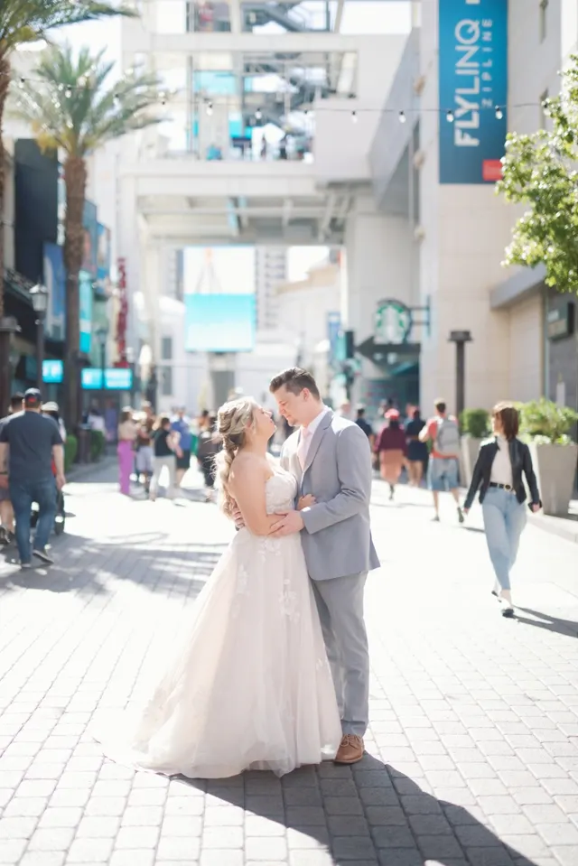 Bride and groom about to kiss in the middle of the LINQ Promenade with storefronts, string lights and the Fly LINQ zipline sign behind them