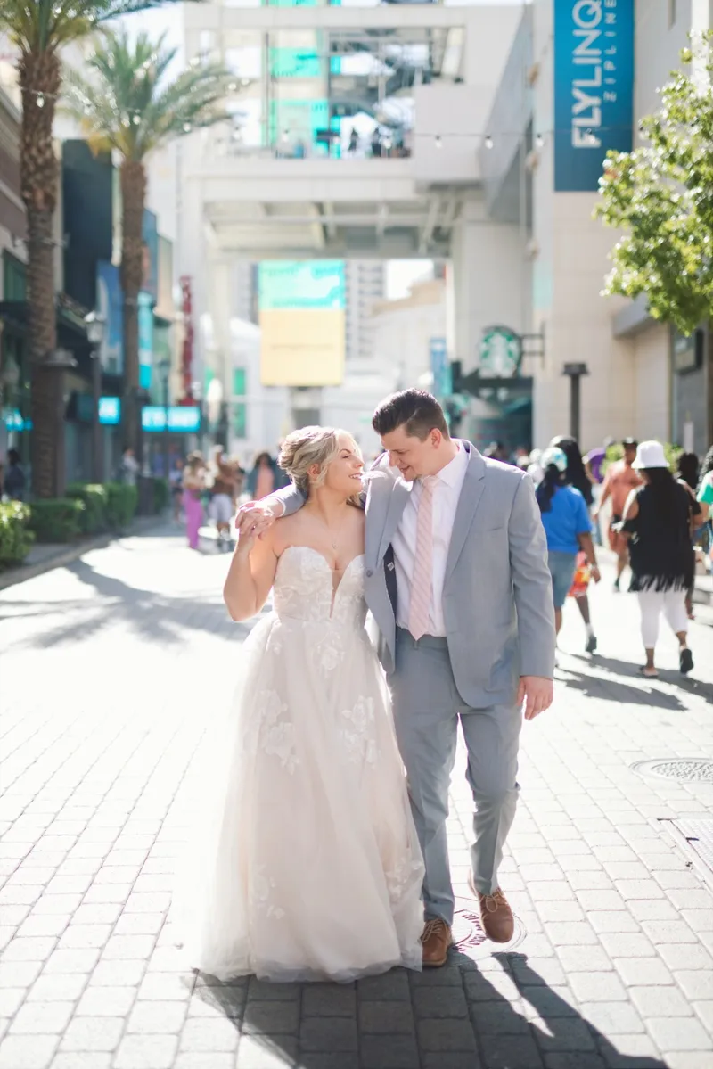 Bride and groom walking the promenade past the shops together, both of them laughing