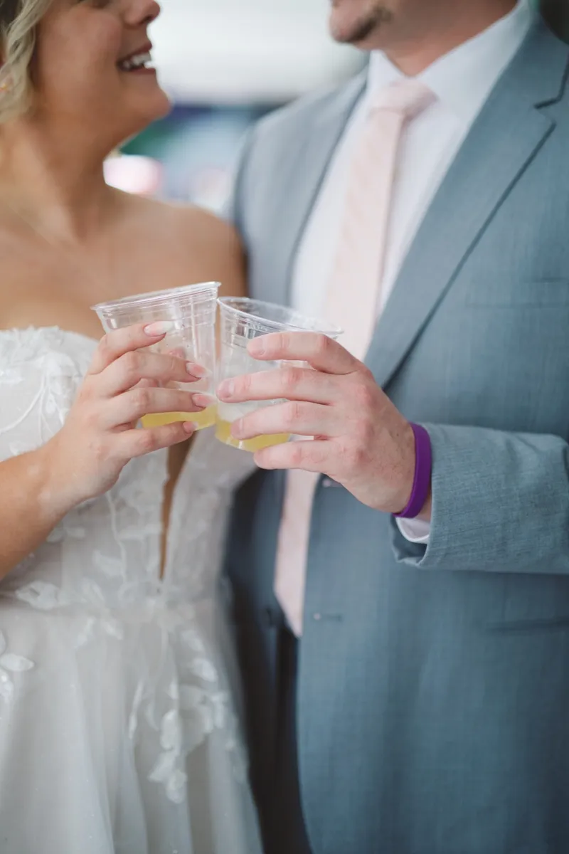 Close frame of the bride and groom touching their cups together, her white lace bodice on one side and his pink tie on the other