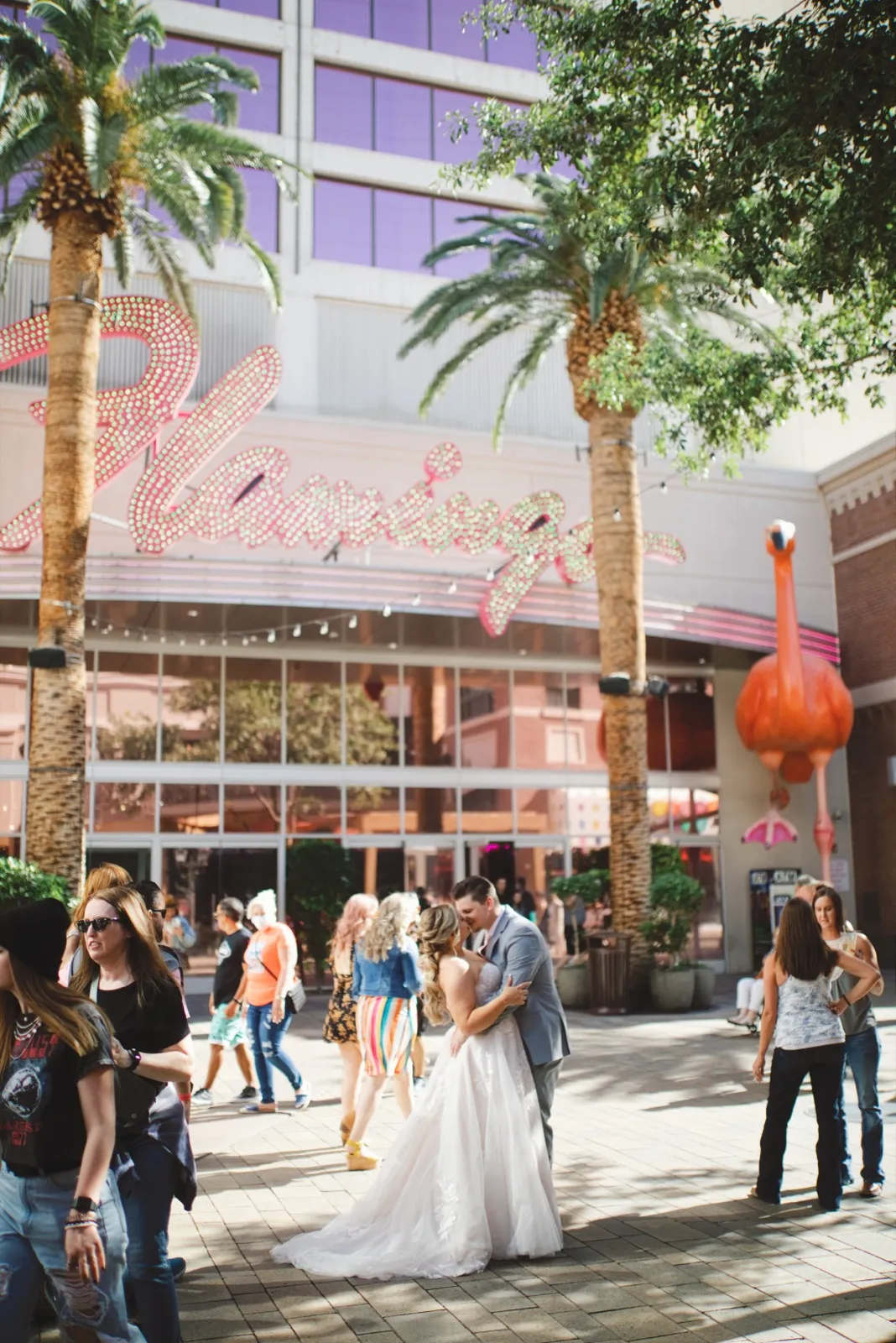 Bride and groom kissing under the Flamingo’s pink neon sign as a crowd of visitors walks past them