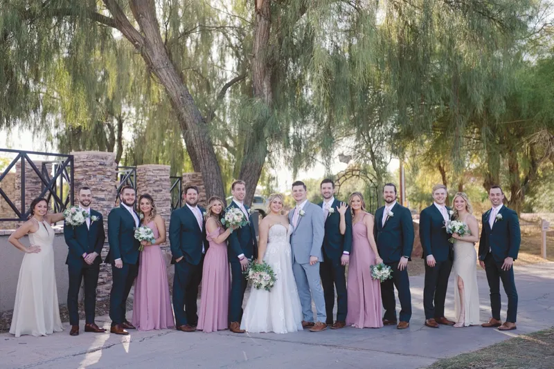 Full wedding party lined up together under the trees, the men in navy and grey and the women in pink