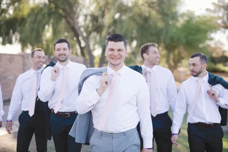 Groomsmen walking together in white shirts and ties with their jackets slung over their shoulders