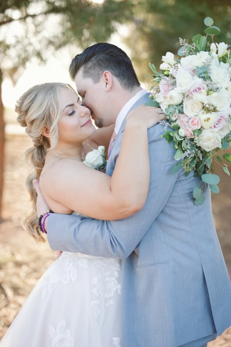 Couple holding each other close with the bride's white and green bouquet raised over his shoulder