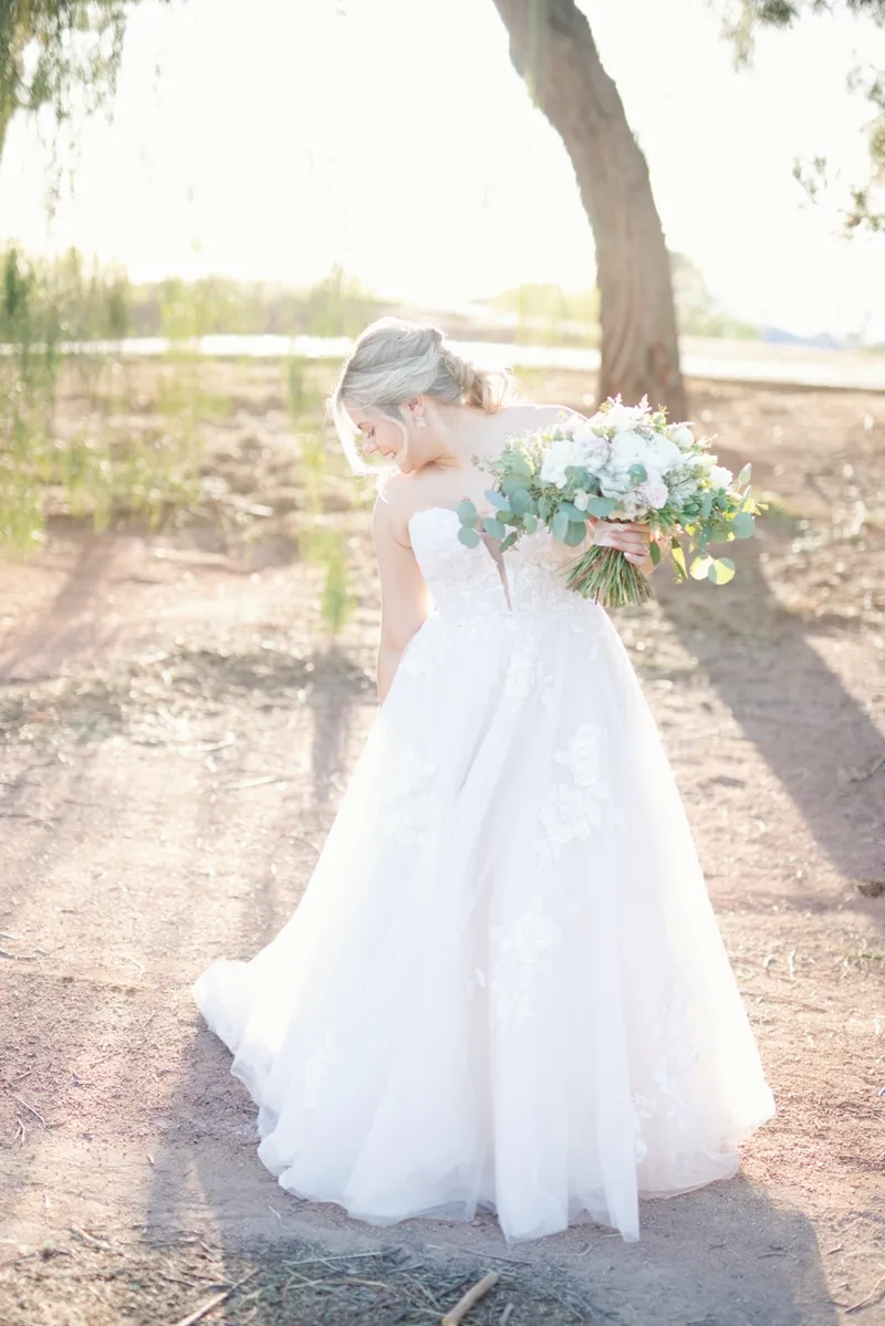 Bride walking the path with her bouquet, backlit by the sun coming through the trees